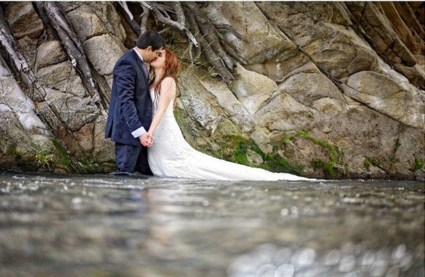 Novios besándose en el agua junto a las rocas